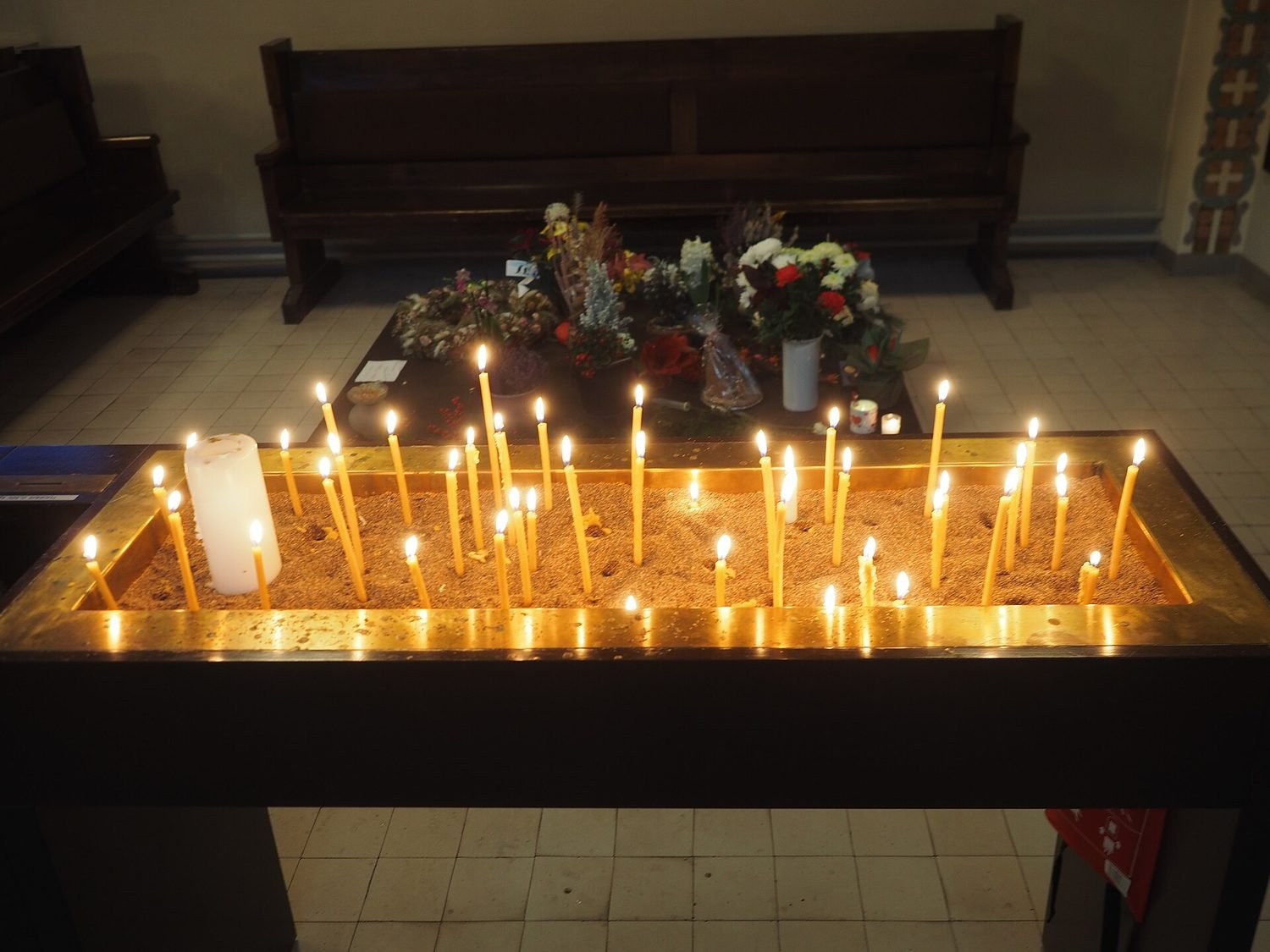 Rangée de cierges allumés sur un porte-cierges, dans la pénombre d'une église